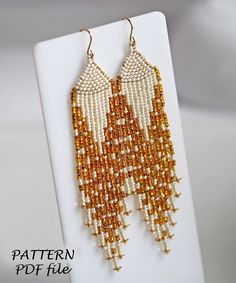 a pair of beaded earrings with gold and white fringes on a white stand