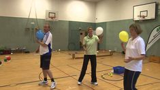 three people in a gym with balls and tennis rackets on the floor, one holding a yellow frisbee