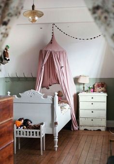 a pink canopy bed sitting next to a white dresser and chest in a child's bedroom