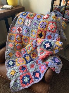 a crocheted granny blanket is sitting on a chair with a pillow in front of it