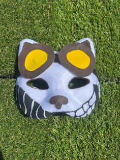 a white mask with yellow eyes and brown ears on the green grass in front of someone's face