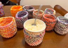 there are many cups that have been made out of knitted material and one has a spoon in it