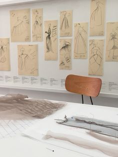 a chair sitting on top of a white table next to drawings and pencils in front of a wall