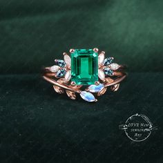 an emerald and diamond ring with leaves on the side, sitting on a black surface