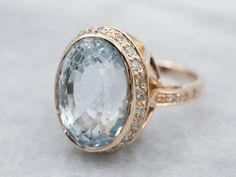 "A perfect sky-blue hue radiates from the center of this classic piece. This oval-cut natural blue topaz has been bezel-set in a halo of glittering diamonds and a frame of polished gold, this halo ring has plenty of light and life and will wear beautifully day or night. Metal: 14K Yellow Gold Gem: Natural Blue Topaz 6.00 Carats Gem Measurements: 16.0 x 11.5 mm, Oval Accents: 30 Diamonds totaling .75 Carats, SI2 in Clarity, G in Color Ring Size: 7.25 Marks: \"14K\" Stamped on the inside band To v Topaz Cocktail Ring, Yellow Gold Cocktail Ring, Diamond Halo Ring, Gold Cocktail Ring, Right Hand Rings, Halo Pendant, Diamond Glitter, Hand Ring, Antique Engagement Rings