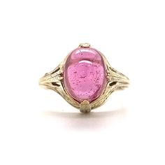 Art Deco Cabochon Cut Pink Tourmaline Ring in 14k Yellow Gold This one of a kind Art Deco ring features a light pink tourmaline in 14 karat yellow gold. The tourmaline reflects a romantic, taffy pink hue. Cabochon cut and smoothly polished. The antique shoulders of the band feature geometric engravings. Decorative and fashionable. Finished in 14 karat yellow gold. This statement cocktail ring is a treasure from the Art Deco era. PRIMARY STONE Stone: Pink Tourmaline Measurements: 10.48 mm x 8.03 Formal Pink Rings With Polished Finish, Pink Round Cabochon Ruby Ring, Pink Cabochon Ruby Ring, 14k Gold Pink Rings With Polished Finish, Elegant Pink Cabochon Ruby Ring, Elegant Pink Ruby Cabochon Ring, Pink Rings With Polished Finish Fine Jewelry, Fine Jewelry Pink Rings With Polished Finish, Pink Wedding Rings With Polished Finish