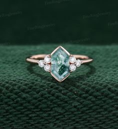 a green and white diamond ring sitting on top of a green cloth