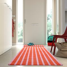 an orange and white striped rug on the floor in front of a door with a red chair