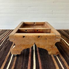 an old wooden box sitting on top of a striped tablecloth covered floor next to a white brick wall