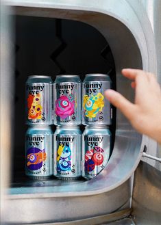 six cans of energy drink are in an industrial type oven, with one hand pointing at the door