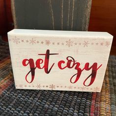 a wooden block with the word get cozy painted on it sitting on a carpeted area