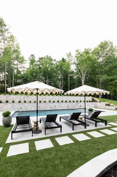 an outdoor dining area with lawn chairs and umbrellas on the grass near a swimming pool