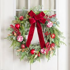 a christmas wreath hanging on the front door with red ornaments and greenery around it