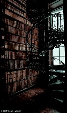 a spiral staircase in an old library with lots of books on the walls and floor