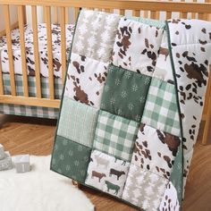 a baby crib with a green and white blanket on it's side, next to a teddy bear toy