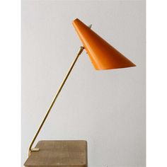 an orange table lamp sitting on top of a wooden desk next to a white wall