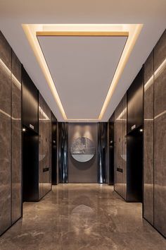 an empty hallway with black elevators and marble flooring is lit by recessed lighting