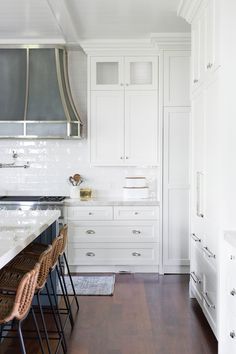 a kitchen with white cabinets and counter tops next to bar stools in front of an oven