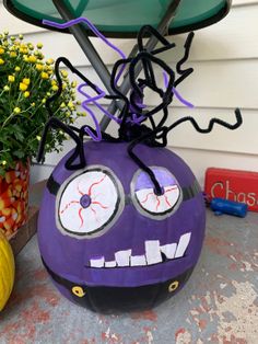 a purple pumpkin decorated with googly eyes and spider webs on its head sitting next to a potted plant