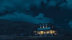 a house is lit up at night with clouds in the sky and mountains behind it