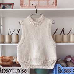 a knitted sweater hanging on a rack in front of yarns and crochet baskets