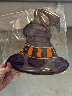 a hand holding a plastic witch hat on top of a bag with orange and black stripes