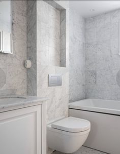 a white toilet sitting next to a bath tub under a window in a bathroom with marble walls