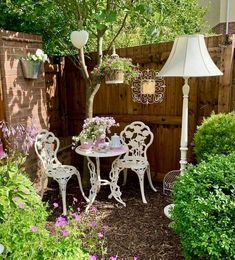 a table and chairs in a garden with flowers on the ground next to a fence