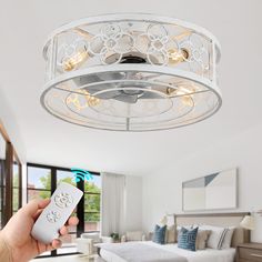 a person holding a remote control in front of a ceiling fan with lights on it