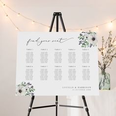 an easel with a seating chart on it in front of a string of lights