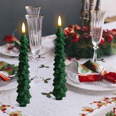 two green christmas trees sitting on top of a table next to glasses and plates with candles