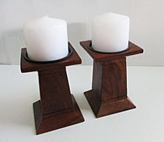 two white candles sitting on top of wooden stands