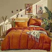 an orange comforter and pillows on a bed in a room with potted plants