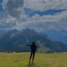 a woman standing on top of a lush green hillside under a cloudy sky with her arms outstretched