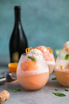 two glasses filled with ice cream and orange garnish next to a bottle of wine