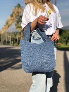 a woman carrying a blue crocheted tote bag with a flower in it