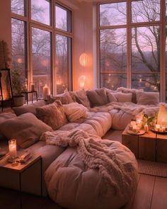 a living room filled with lots of furniture and candles on top of the tables in front of large windows