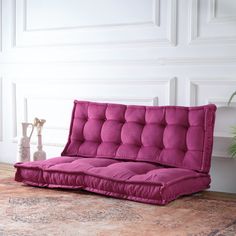 a futon sofa bed sitting on top of a rug in front of a white wall