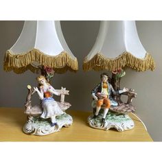 two figurines sitting on top of a wooden table next to lamps with tassels