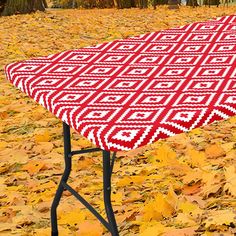 a red and white table cloth sitting on top of a black ironing board covered in leaves