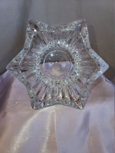 a clear glass dish sitting on top of a white satin covered table cloth with a circular hole in the center