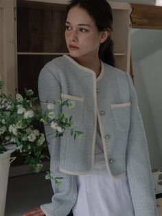 The individual is wearing a textured jacket with a contrasting trim that outlines the neckline, placket, and pocket flaps, providing a chic accent to the design. The jacket features a round neck, a straight-cut opening, and a series of buttons down the front for closure. The pockets are placed at chest and waist level, offering both functional and aesthetic elements. The light color and the distinctive texture of the fabric suggest a spring or summer garment, appropriate for both casual and semi-formal occasions.- The jacket's classic tailoring and detailing give it a timeless elegance.- It could be paired with various outfits due to its light color and simple yet sophisticated style.- The texture of the jacket adds depth to the garment, making it a statement piece while maintaining a subt Blue Tweed Jacket, Aesthetic Elements, Jacket Formal, Light Blue Jacket, Classic Tailoring, Textured Jacket, Blue Tweed, Contrasting Trim, Spark Joy