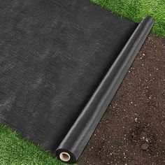 a roll of black tarp laying on top of green grass next to a patch of dirt