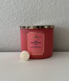 a pink candle sitting on top of a table next to a white wall with a silver lid