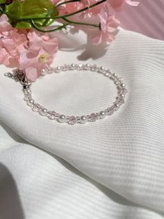 a close up of a bracelet on a white cloth with pink flowers in the background