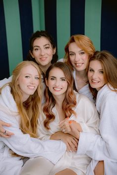 four beautiful young women wrapped in white robes posing for the camera with their arms around each other