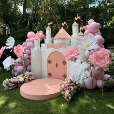 a pink and white castle surrounded by flowers, balloons and other decorations in the grass