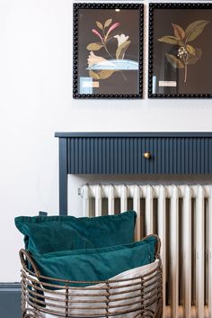 a radiator with two pictures on the wall above it and a basket next to it