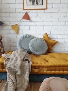 a bed with pillows and blankets on it in front of a white brick wall,