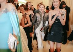 two women standing next to each other in front of a group of people wearing evening gowns